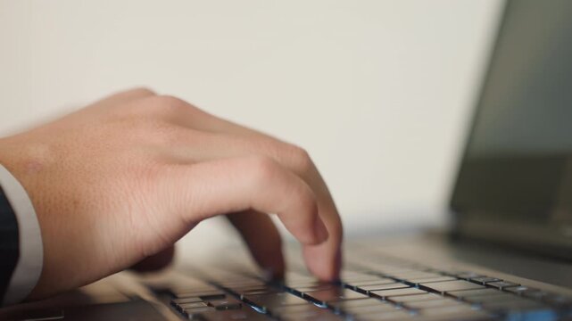 Closeup hands typing on laptop keyboard, focused executive at office desk, rapid keystrokes, shallow depth of field, soft natural lighting, modern black laptop, suit cuff visible, professional