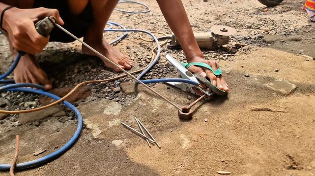 Sidoarjo, Indonesia - 30 may, 2026: Close up of Manual Stick Welding Process Outdoors, Man Fusing Metal Parts on Dirt Ground with Bright Sparks and Smoke