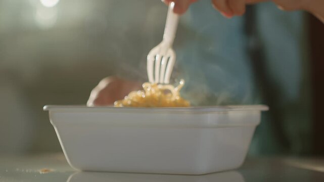 Office lunch scene with steaming container, plastic fork probing hot rice under soft daylight, hand in blue sleeve retrieving bite, tabletop reflection and rising steam, quick midday break mood