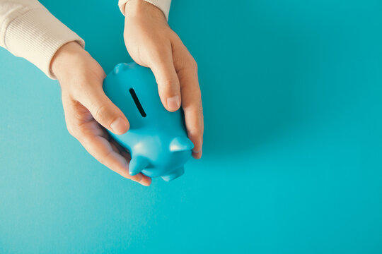 Woman hand holding blue piggy bank on blue background, top view