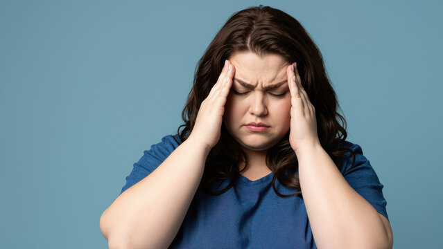 Headache Distress: A woman, exhibiting signs of discomfort, clasps her temples, her brow furrowed in pain, conveying the isolating experience of a severe headache.