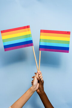 Two hands holding rainbow flags against a light blue background.