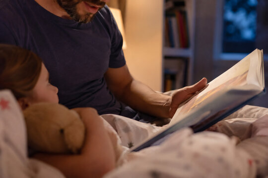 Father reading bedtime story to little girl in cozy bedroom at night