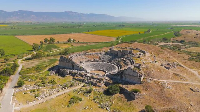 Balat, Turkey. Miletus Theatre, ancient stone amphitheater built into a hillside, aerial panoramic view over green agricultural plains and distant mountains under a clear blue sky. Aerial View, Maste