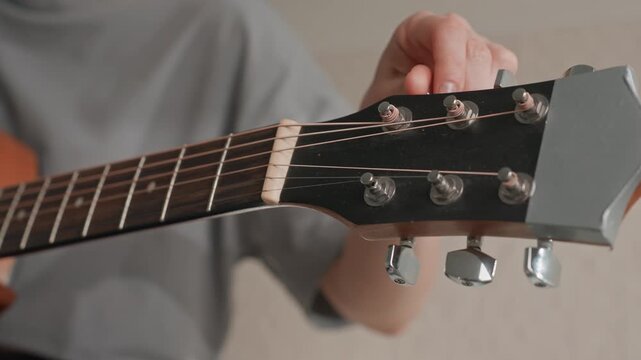 Caucasian woman tuning guitar headstock closeup, fingers adjusting pegs with careful focus, indoor home practice, warm wood tones and metal tuners, concentrated musician preparing song, soft natural