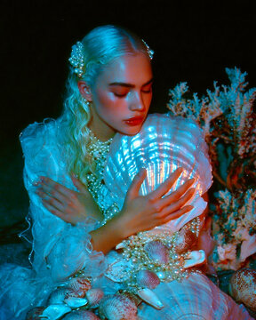 londe woman holding glowing seashell surrounded by pearls and coral in dark underwater fantasy