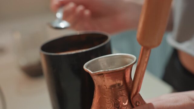 Closeup of white hands stirring cezve, copper pot beside black canister, spoon measuring grounds and adding to pot, warm morning light, tactile brewing ritual by home barista, fragrant aroma