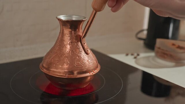 Closeup copper cezve on stove, hand stirring dark grounds and foam, red heating element glowing, hammered metal texture, traditional coffee preparation, quiet kitchen countertop scene, warm steam