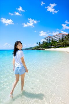 Young Japanese Woman Walking on a Tropical Beach and Looking Back at a Luxury Resort