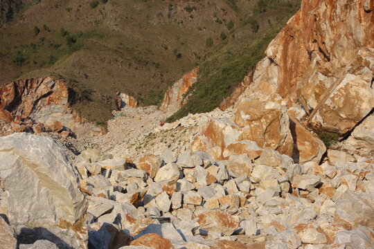 Looking down into a massive marble rock extraction valley in Pakistan, filled with an extensive field of shattered boulders and blasted stone aggregates below a green hillside.