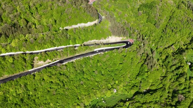 Top down aerial drone view of winding mountain highway through dense green forest with cars 4K.