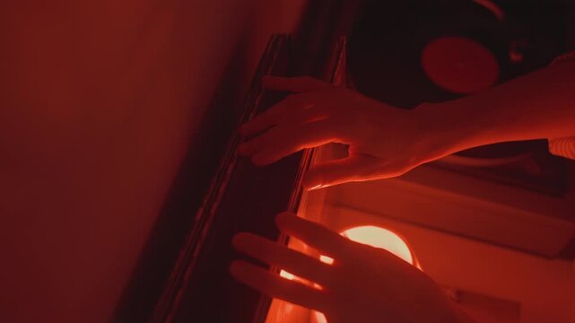 Red glow white woman flipping vinyl sleeve in closeup, hands sorting record collection beside glowing lamp and turntable, tactile search and curator vibe, late night DJ and listener ritual, nostalgic