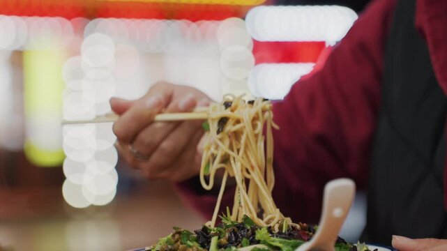Closeup asian hands picking noodles with chopsticks from steaming bowl at night colorful bokeh neon lights, quick slurp and bite, foodie traveler enjoying street stall fare, cinematic shallow focus