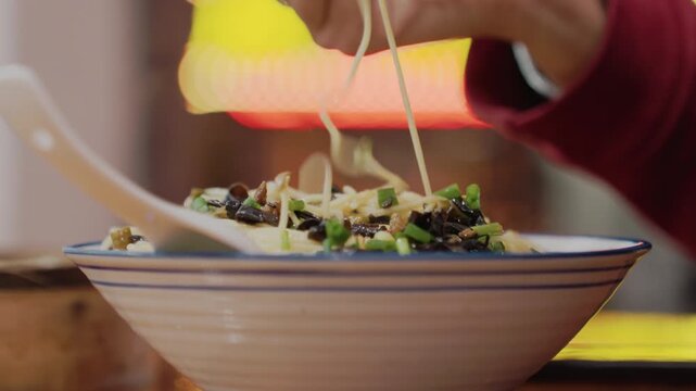 Latenight bowl of noodles, neonlit stall hands use chopsticks to lift steaming ramen topped with scallion and sesame, ceramic bowl on wooden table, warm cozy urban street food atmosphere with blurred