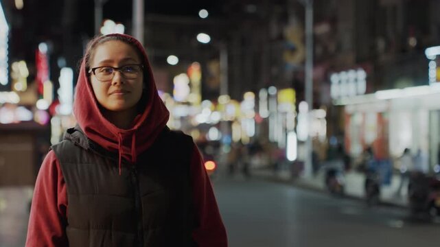 Night street smile woman artist hoodie glasses, hopeful stroll under neon illumination, warm storefront glow and soft bokeh, casual jacket, gentle gaze across traffic, candid joyful moment in city