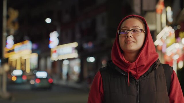 Night street gaze woman hoodie glasses, quiet upward glance toward city lights, calm reflective mood with neon glow and soft bokeh, still sidewalk moment, hopeful expression in downtown night