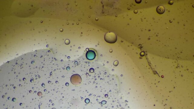 Abstract macro footage of scattered drops and a distinct blue-centered bubble on a yellow fluid background