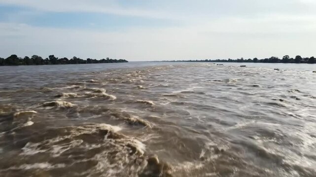 Wide view of choppy river water flowing with trees along the distant banks under a blue sky