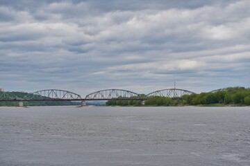 Fototapeta premium Steel arched bridge over a wide river under cloudy dramatic sky
