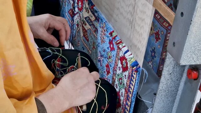 Close-up of a female artisan's hands knitting yarn and weaving an authentic traditional oriental rug on a vertical loom. Concept of cultural heritage, craftsmanship, and handmade textile art