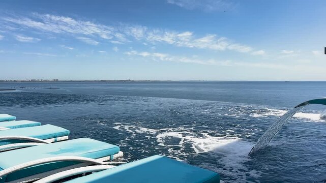 Infinity pool with blue lounge chairs and water fountain overlooking the Black Sea under a clear sky