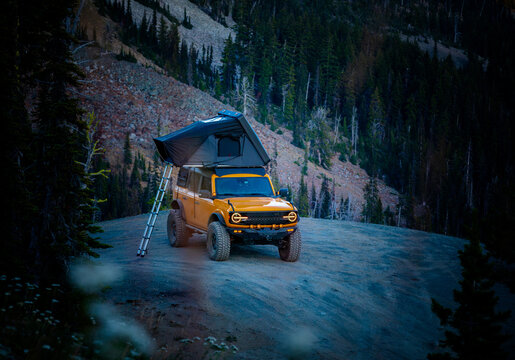 Orange offroad SUV with rooftop tent camping in the mountains