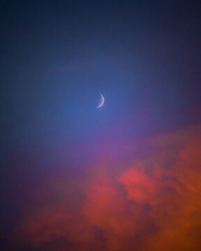 Waxing crescent moon above vibrant sunset clouds