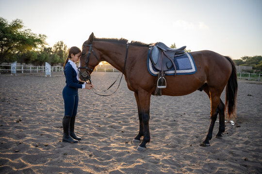Young rider and her brown horse at sunset