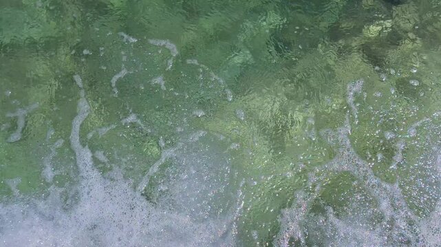 Top-down view of clear, greenish sea water with gentle waves and white foam