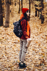 Fototapeta premium Woman stands in autumn forest holding thermos. wilderness survival skills, outdoor escape plan, off-grid living preparation.