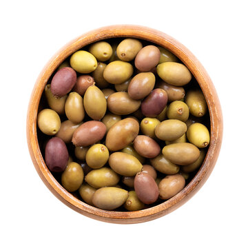 Taggiasca olives with stone, colorful mix of small Italian olives in a wooden bowl. Whole, unripe, cured green olives, and ripe, purple olives, preserved in brine. Isolated close-up, from above. Photo