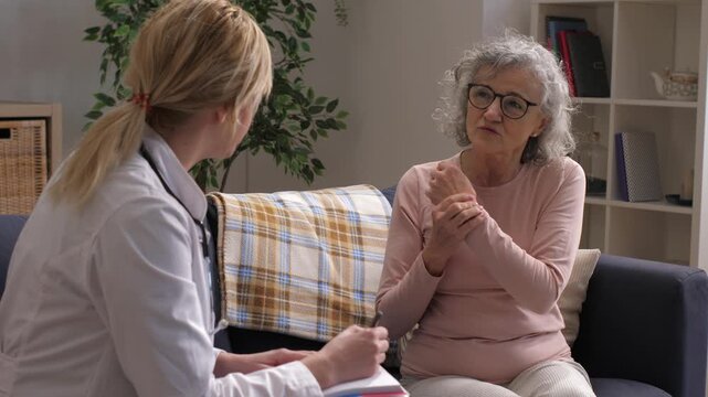 Senior woman complaining about wrist pain to doctor during home visit