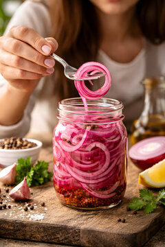 Pickled red onion rings lifted from glass jar, homemade fermented vegetables, gourmet condiment preparation, healthy preserved food, vibrant purple onion pickle, culinary recipe ingredient, rustic kit