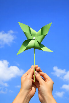 Green paper pinwheel held in hands against blue sky, eco friendly windmill craft toy, sustainable energy concept, renewable power symbol, outdoor childhood creativity, environmental innovation, clean 