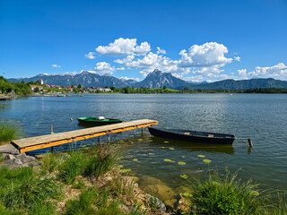 Obraz premium Germany, Two moored rowboats on lakeside pier with Hopfen am See village in background