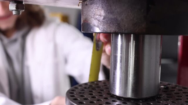 Close-up of hydraulic press piston with blurred engineer working in background