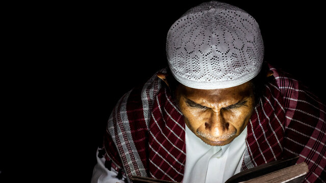 a muslim man is reading the quran at night