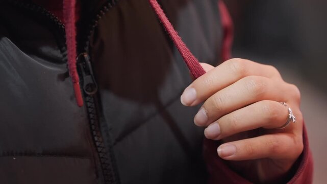 Night walking hoodie string close up soft bokeh streetlight close up on hands adjusting drawstring of padded jacket ring on finger subtle nail polish chilly evening mood slow walking pace