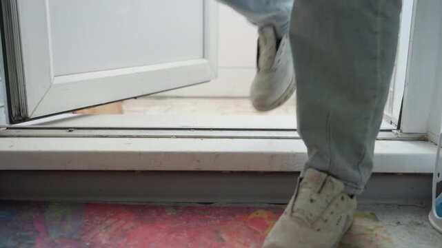 Stepping into pottery workshop, paintstained threshold and worn sneakers crossing doorway, denim trousers dusted with glaze and paint, colorful splatter on floor, soft daylight from outside, quiet