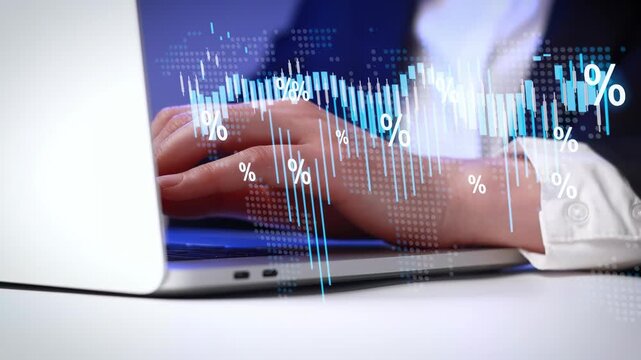 Person types on laptop while financial data displays on screen in office setting during working hours.