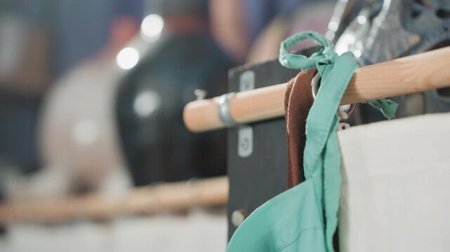 Caucasian artisan arranges hanging aprons calmly, teal and brown fabric against painted wall, ceramic vases blurred on shelf, shallow depth and soft bokeh evoke peaceful studio moment