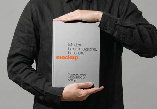 Hardcover Book Mockup Held With Both Hands By Man Front View On Gray Background