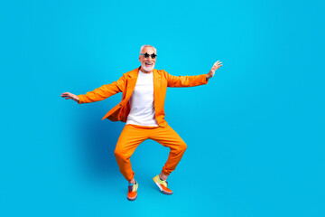 Fototapeta premium Senior man in bright orange suit dancing and smiling on blue background, joyful active lifestyle and colorful fashion portrait