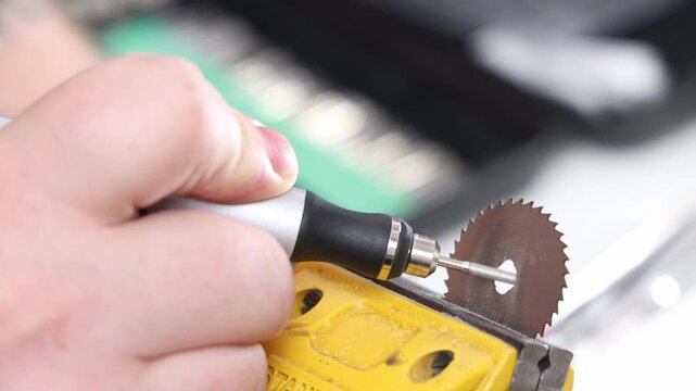 Close up of a hand using a precision rotary tool with a circular saw blade for grinding a small model part in a vise
