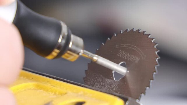 Close up of a hand using a precision rotary tool with a circular saw blade for grinding a small model part in a vise