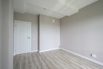 Fototapeta premium A spacious empty room with light grey textured walls, light wood laminate flooring, white baseboards, a white door, and built-in electrical outlets; ready for furnishing