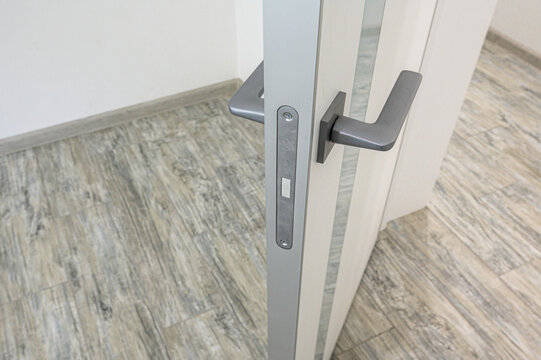modern interior door with a sleek matte grey handle and matching lock plate, set against light-colored walls and grey-beige wood-effect laminate flooring