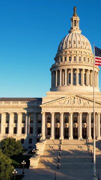 4th of July aerial drone shot over American flag waving on capitol building dome at sunrise, vast blue sky, patriotic cityscape b-roll for Independence Day