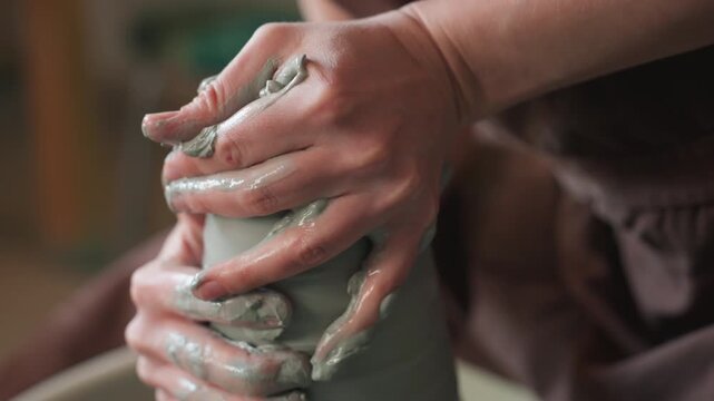 Craftsman skillfully molds wet clay. Detailed shot of hands working with wet clay on wheel. Focused studio image capturing hands meticulously shaping ridged moist clay on spinning wheel