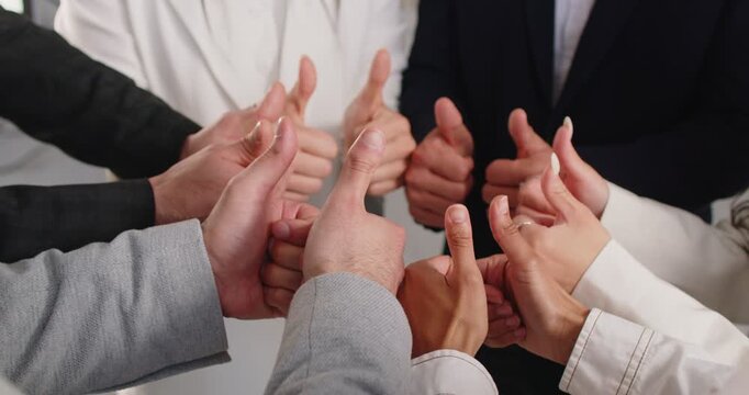 Business people join hands in thumbs up gesture, confident professional entrepreneurs group standing together. Corporate company team of office workers showing focus on goal and friendship, teamwork